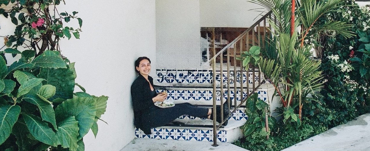 Reanna Kuiken, owner and chef of Hot Chick, sitting on tiled steps holding one of her sandwiches